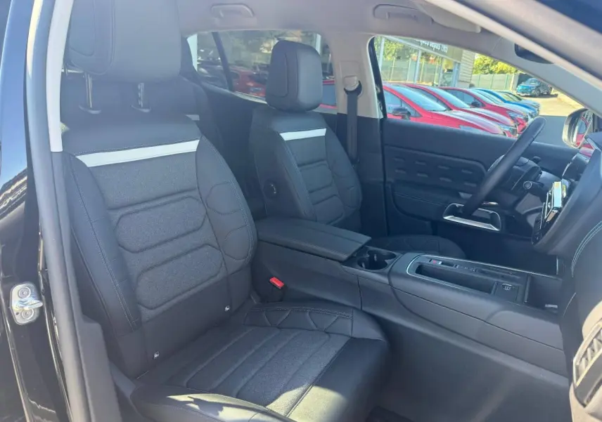 Vue intérieure côté avant gauche du Citroën C5 Aircross noir Perla Nera, sièges tissu et cuir noir avec accoudoir central.