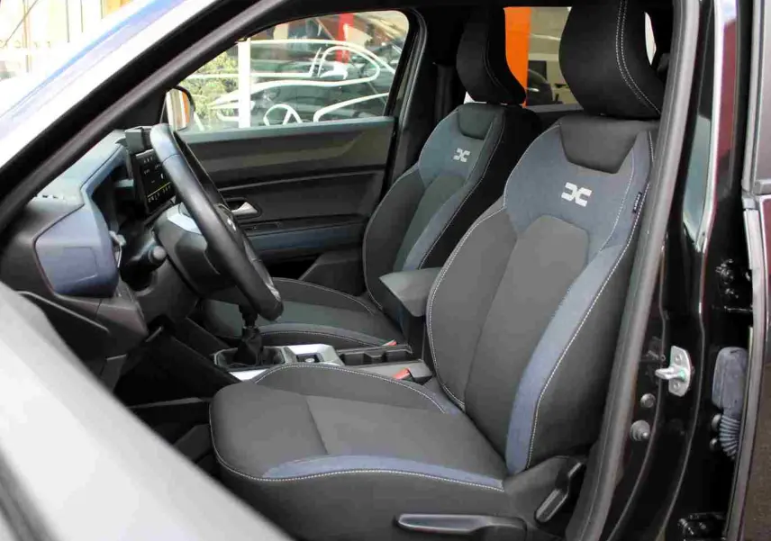 Vue intérieure côté conducteur du Dacia Duster noir 2025, mettant en valeur les sièges avant Denim avec logo Dacia.