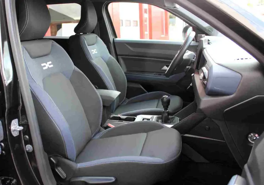Vue intérieure côté gauche du Dacia Duster III noir, mettant en valeur les sièges avant Denim avec logo Dacia.