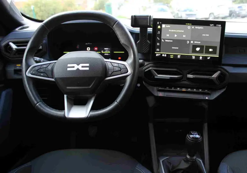 Vue intérieure centrée sur le volant et la console centrale du Dacia Duster 2025, avec écran tactile et levier de vitesses manuel.