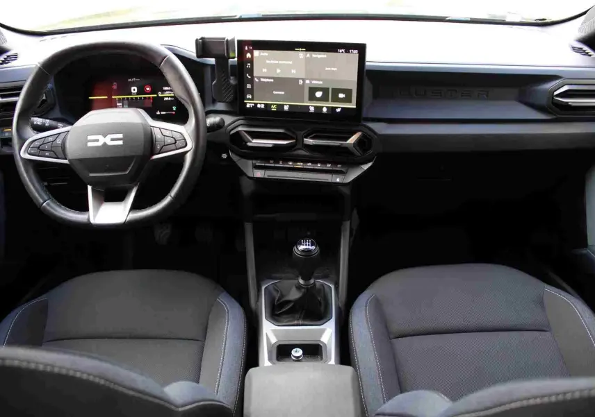 Vue intérieure avant du Dacia Duster 2025 avec tableau de bord numérique, volant soft feel et sellerie Denim bleu.