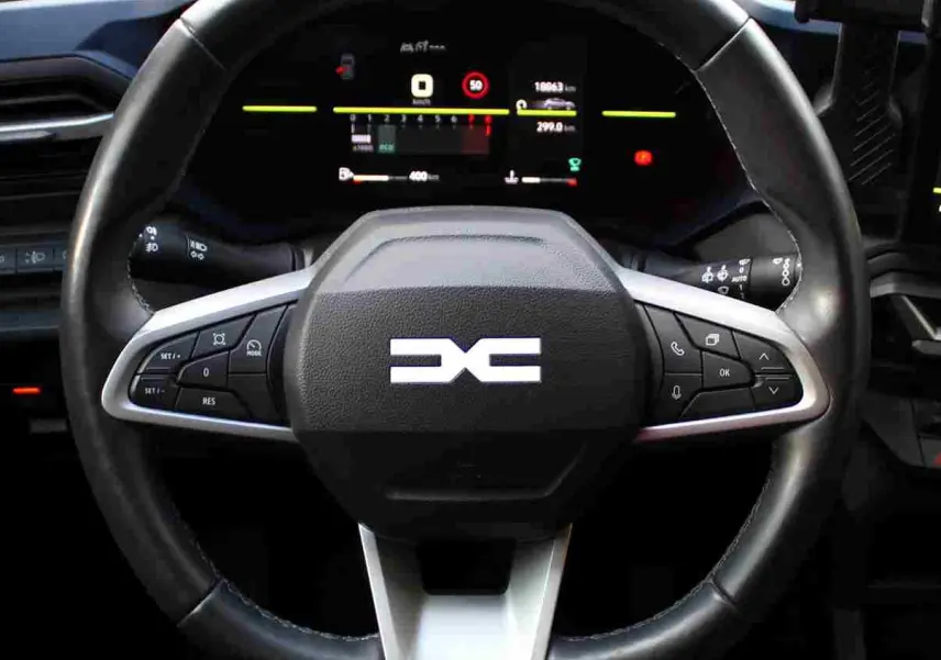 Vue rapprochée du volant noir de la Dacia Duster 2025 avec commandes intégrées et tableau de bord digital.
