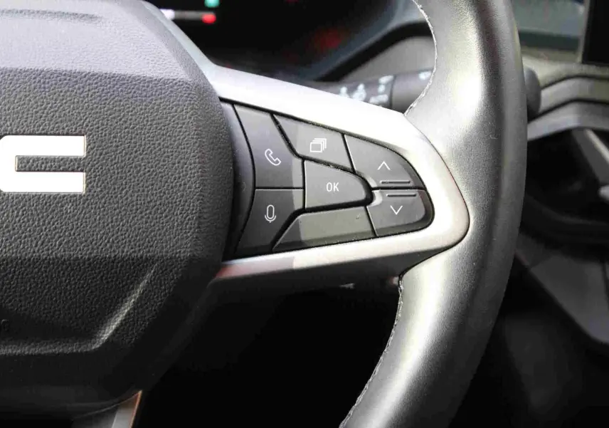 Gros plan sur le volant noir du Dacia Duster 2025 avec commandes multifonctions et finition argentée.