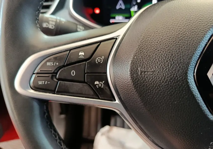 Gros plan sur les commandes à gauche du volant cuir noir de la Renault Clio Techno TCe 90 rouge 2024.