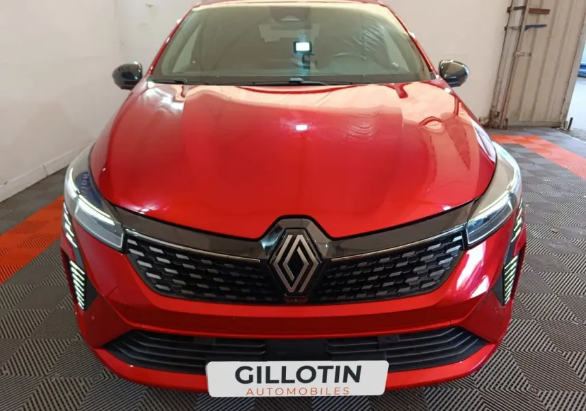 Vue frontale d'une Renault Clio Techno TCe 90 rouge avec calandre noire et feux LED allumés en intérieur.