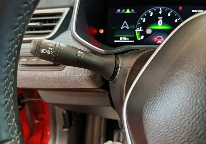 Gros plan sur le combiné d'instruments numérique et la commande des phares à gauche du volant d'une Renault Clio rouge 2024.