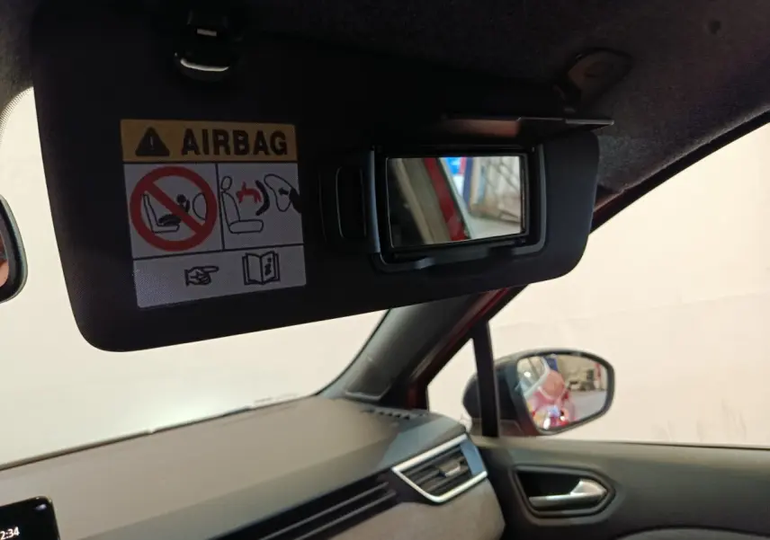 Miroir de courtoisie ouvert sur pare-soleil côté conducteur de Renault Clio rouge, tableau de bord et rétroviseur visibles.