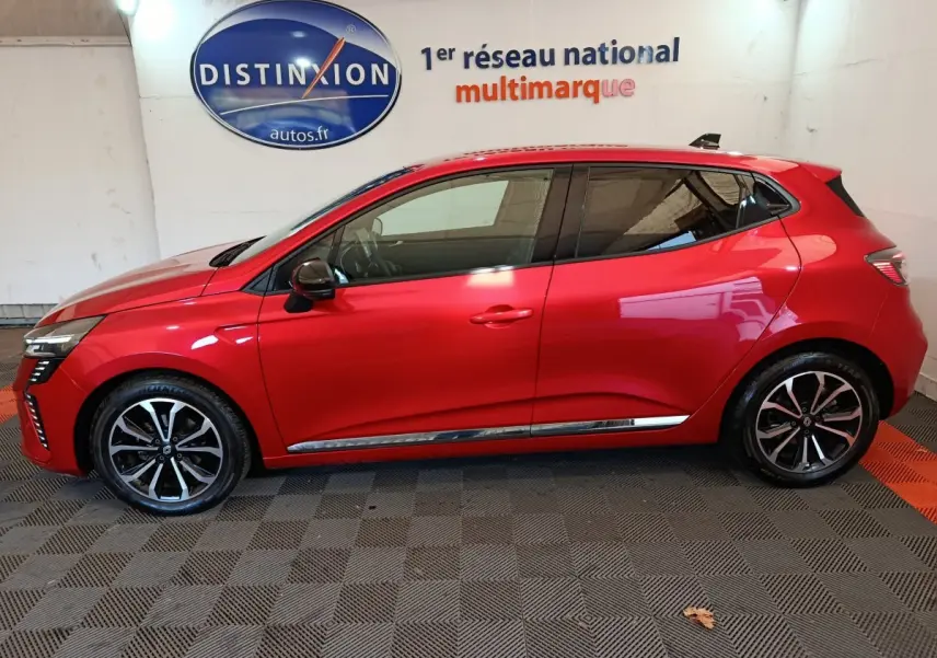 Profil côté gauche d'une Renault Clio Techno TCe 90 rouge 2024 avec jantes alliage et rétroviseurs noirs dans un showroom.