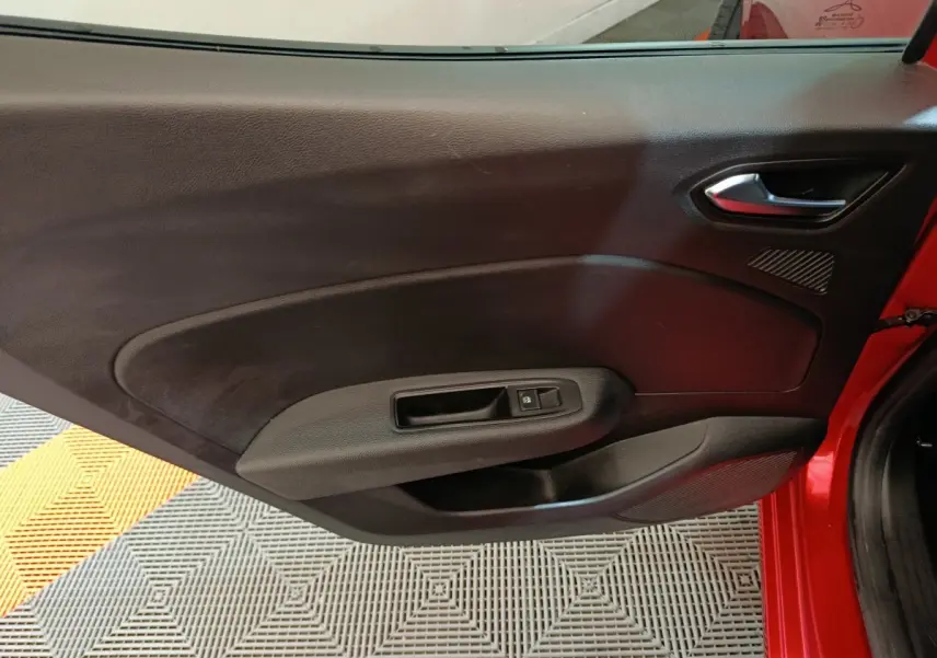 Vue intérieure du panneau de porte côté gauche de la Renault Clio Techno TCe 90 rouge, avec poignée et commande de vitre.
