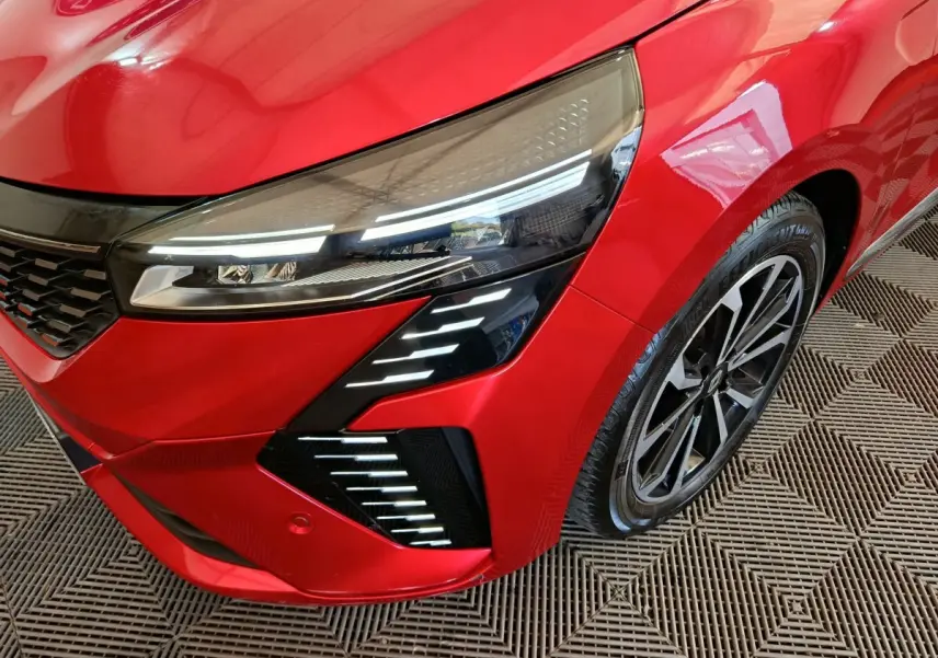 Gros plan sur l'avant droit rouge de la Renault Clio 2024 avec phares LED et jante alliage distinctive.