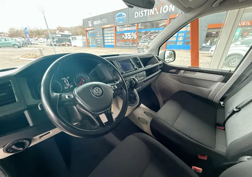 Vue intérieure côté conducteur du Volkswagen Transporter blanc 2018, montrant le volant, tableau de bord et sièges avant.