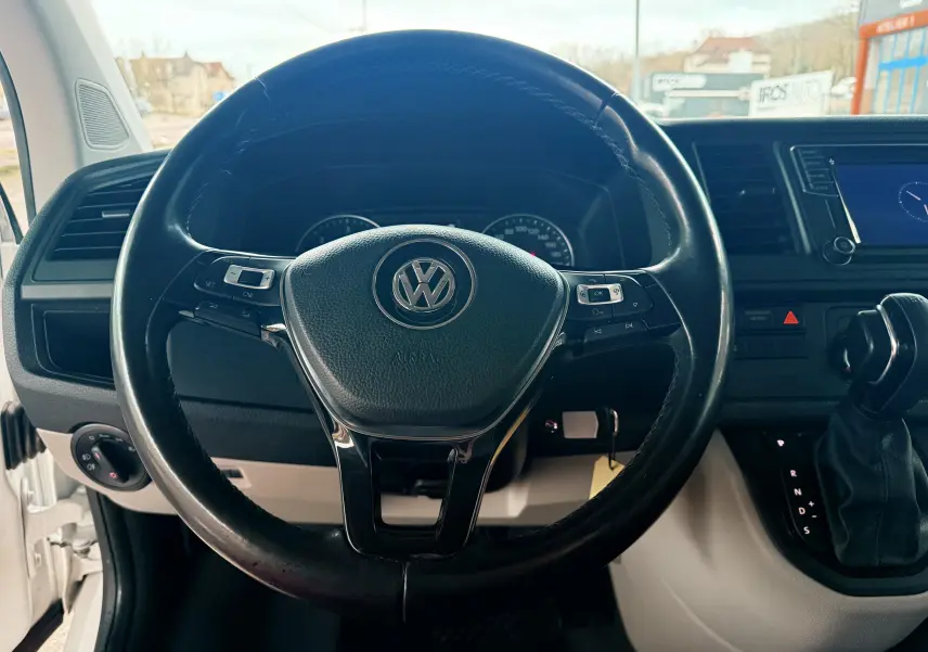 Vue rapprochée du volant noir et du tableau de bord du Volkswagen Transporter blanc, avec levier de vitesses automatique visible.