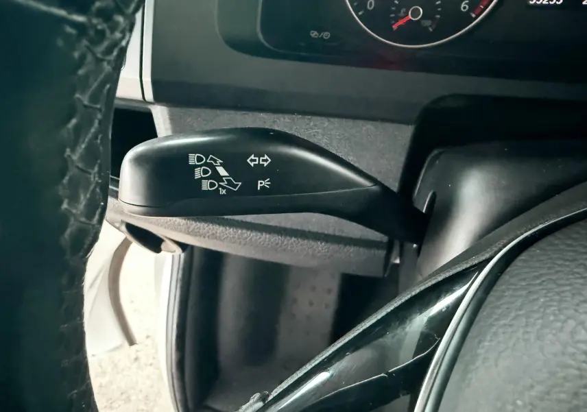 Gros plan sur la manette de clignotants noire à gauche du volant du Volkswagen Transporter blanc, tableau de bord en arrière-plan.