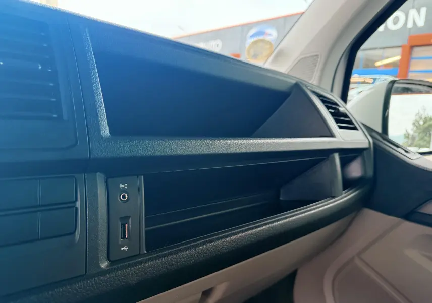 Vue intérieure côté passager du tableau de bord noir du Volkswagen Transporter blanc, avec prise USB visible.