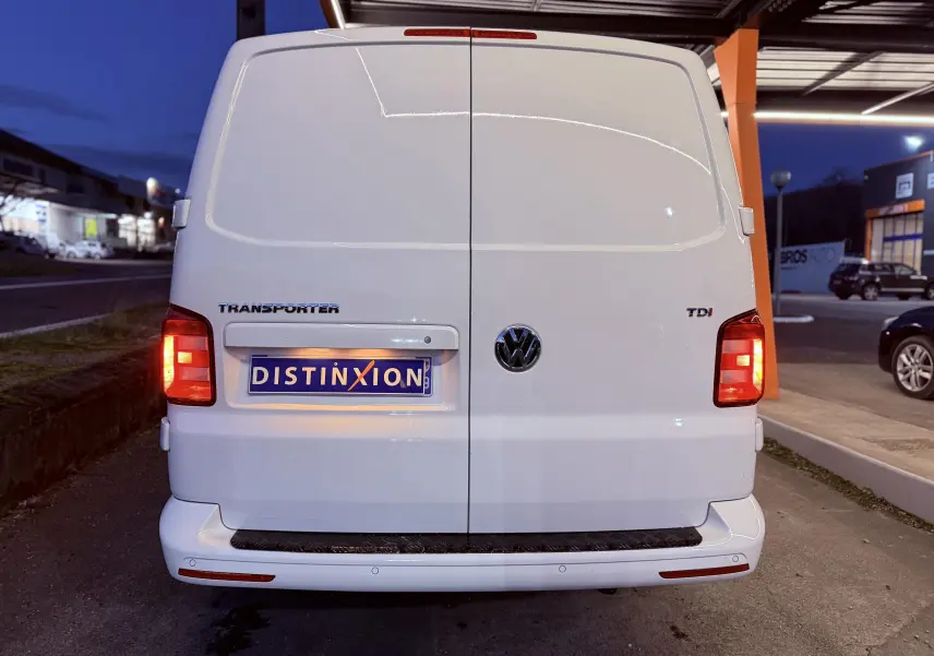 Vue arrière d’un Volkswagen Transporter blanc L1H1 2.0 TDI 150 avec feux allumés et plaque Distinxion.