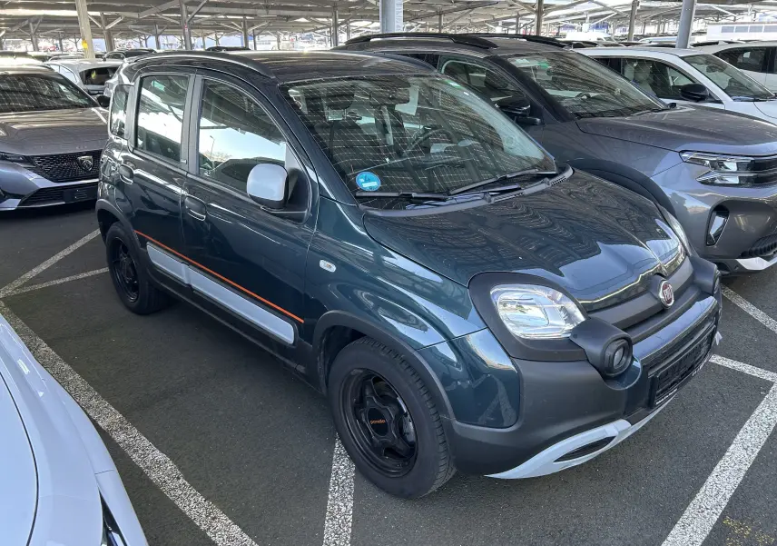 Vue 3/4 avant droite d'une FIAT Panda City Cross 2023 gris minuit avec bande orange et jantes noires en parking couvert.