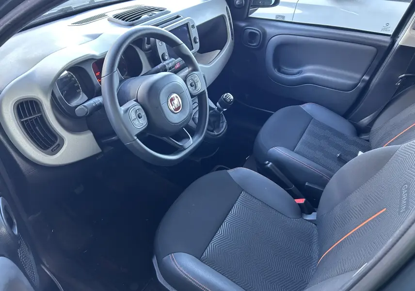 Vue intérieure côté conducteur de la Fiat Panda City Cross 2023, sièges tissu gris avec surpiqûres orange et volant multifonction.