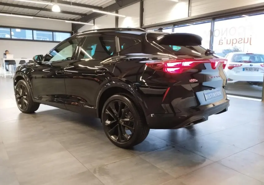 Vue 3/4 arrière droite du CUPRA Formentor noir métal avec jantes noires et feux arrière allumés en intérieur showroom.
