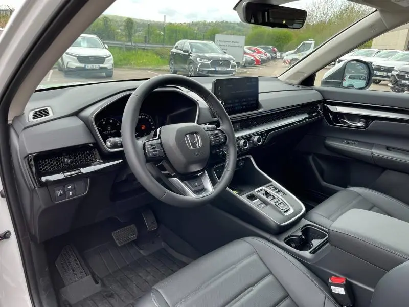 Vue intérieure côté conducteur du Honda CR-V 2024 blanc nacré, avec tableau de bord moderne et sièges cuir noirs.