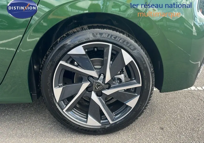 Gros plan sur la roue avant droite d'une Peugeot 308 2024 vert olivine métal avec jante alliage bicolore moderne.