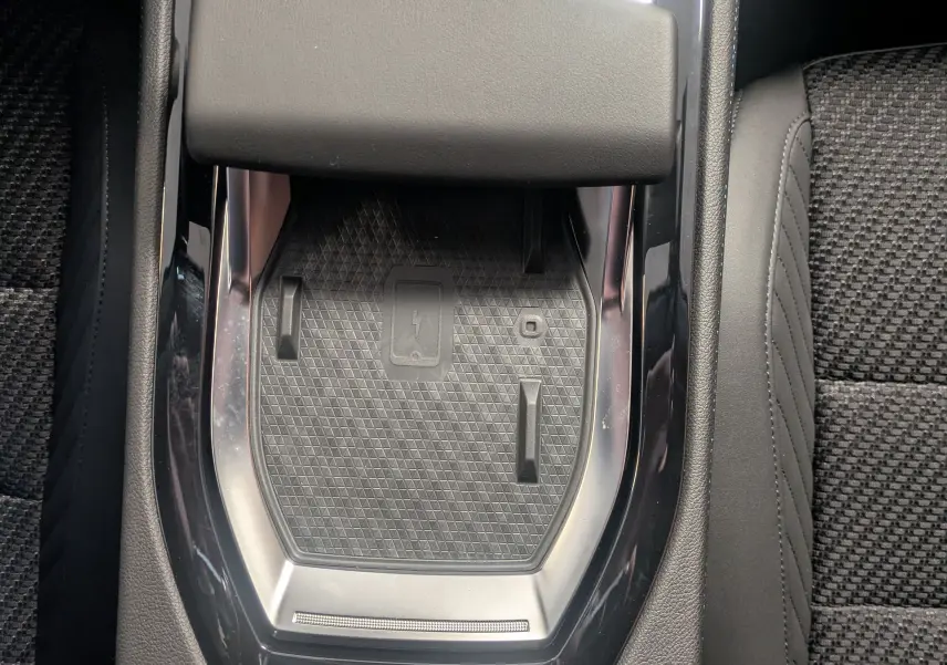 Gros plan sur la console centrale noire du Renault Austral Ph.2 E-TECH 200 avec surface de charge sans fil et accoudoir cuir.