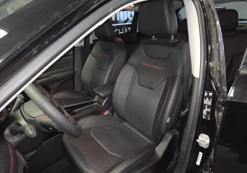 Intérieur avant du Jeep Compass Trailhawk 2024 noir, sièges cuir noirs avec logo Trailhawk rouge visible sur les appuie-têtes.