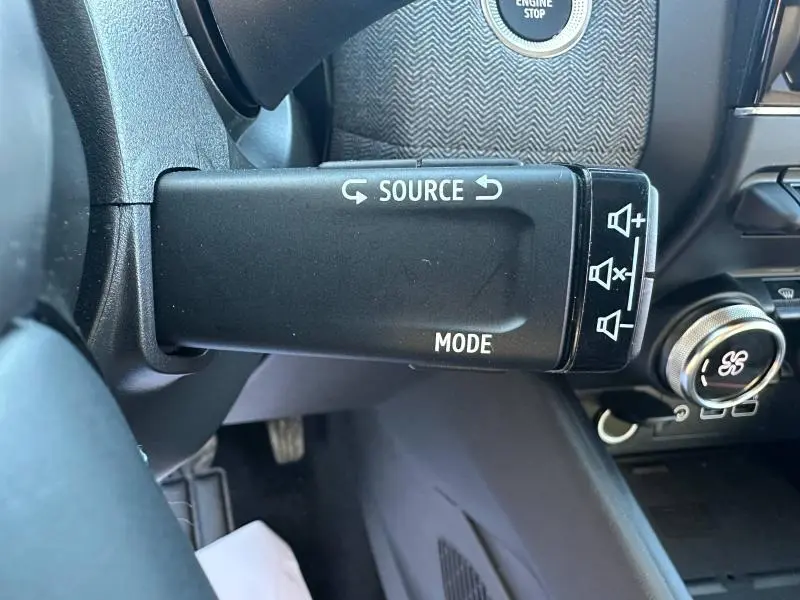 Gros plan sur la commande au volant gauche de la Renault Clio 1.6 E-Tech 145ch rouge, avec boutons source et mode visibles.