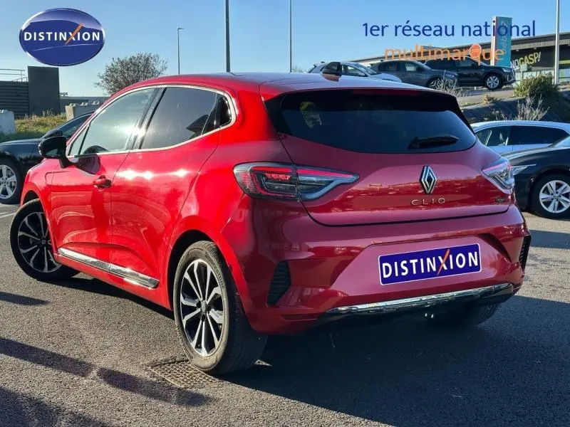 Vue 3/4 arrière droite d'une Renault Clio 1.6 E-Tech 145ch full hybrid rouge flamme avec jantes alliage et vitres teintées.