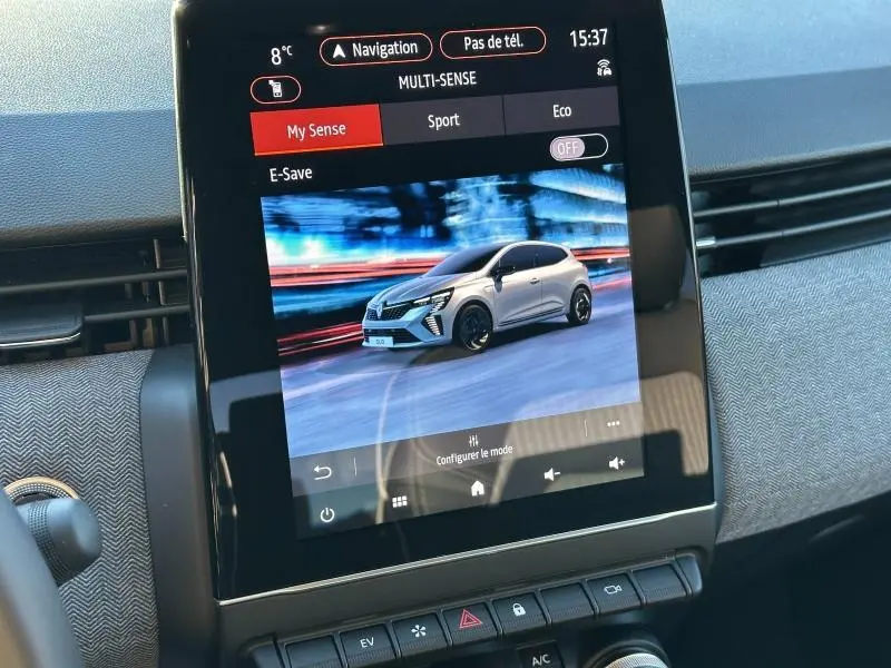 Écran tactile intérieur montrant une Renault Clio blanche en 3/4 avant sur fond flouté, mode de conduite Multi-Sense.