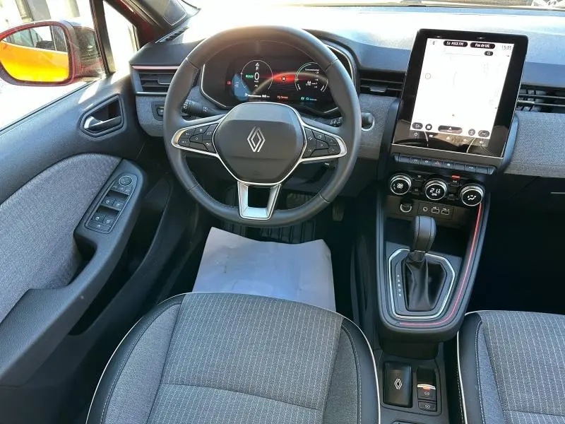 Vue intérieure avant centrée sur le volant Renault, tableau de bord numérique et écran tactile vertical de la Clio 1.6 E-Tech hybride.