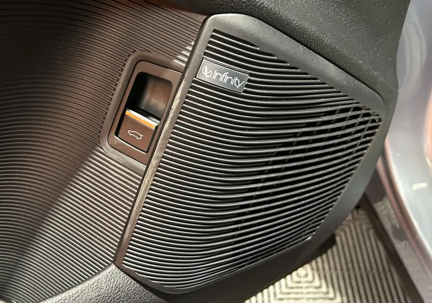 Détail intérieur du haut-parleur audio Infinity et bouton d'ouverture du hayon sur la porte côté conducteur du BYD SEAL U gris.
