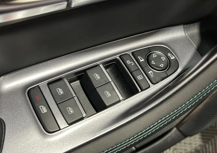 Gros plan sur les commandes de lève-vitres et rétroviseurs côté gauche avec surpiqûres bleu-vert sur cuir noir.