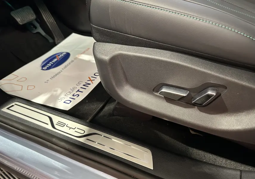 Gros plan sur les commandes de réglage du siège côté gauche et la plaque de seuil BYD dans l'habitacle noir.