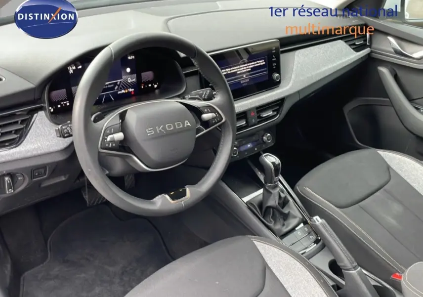Vue intérieure du poste de conduite du Skoda Kamiq blanc glacier 2025, avec volant multifonction et écran tactile central.