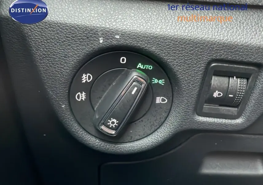Gros plan sur le bouton de commande des phares du Skoda Kamiq blanc glacier, avec réglage automatique activé.
