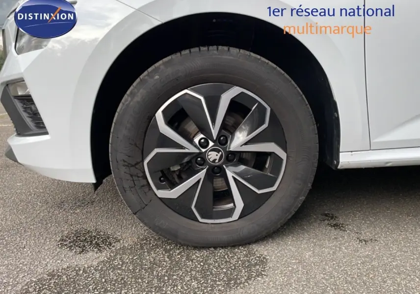 Gros plan sur la roue avant gauche d'un Skoda Kamiq blanc glacier avec jante noire et argentée au design moderne.