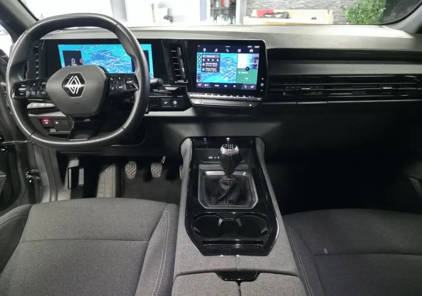 Vue intérieure avant du Renault Austral gris, mettant en valeur le volant multifonction, l'écran tactile central et la boîte manuelle.