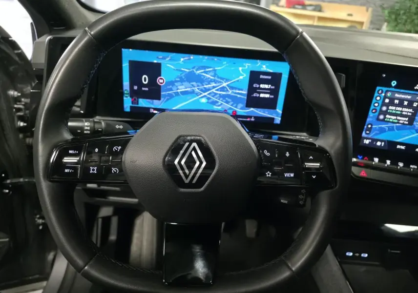 Vue rapprochée du volant noir de la Renault Austral 2024 avec écran numérique et tableau de bord tactile lumineux.