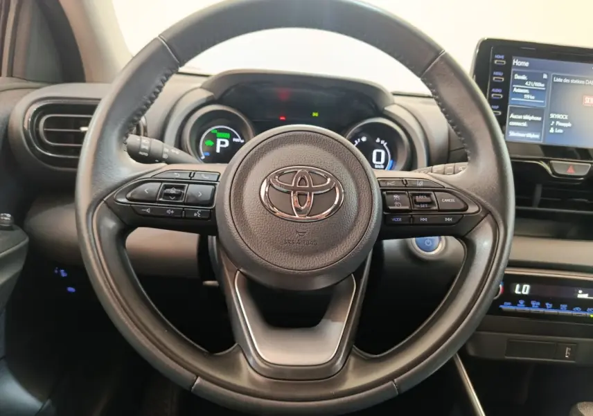 Vue rapprochée du volant cuir multifonctions noir de la Toyota Yaris Hybride 116h avec tableau de bord digital et écran tactile.