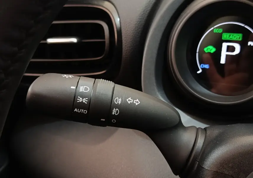 Gros plan sur la commande des phares et clignotants à gauche du volant dans l’habitacle noir de la Toyota Yaris hybride 2023.
