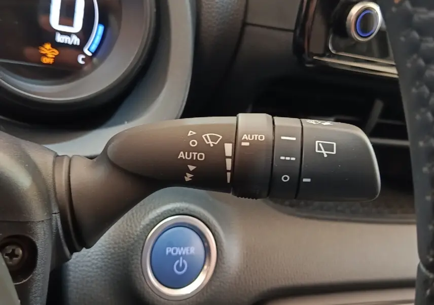 Gros plan sur la commande d’essuie-glace automatique et bouton Power bleu du tableau de bord d’une Toyota Yaris hybride gris clair 2023.