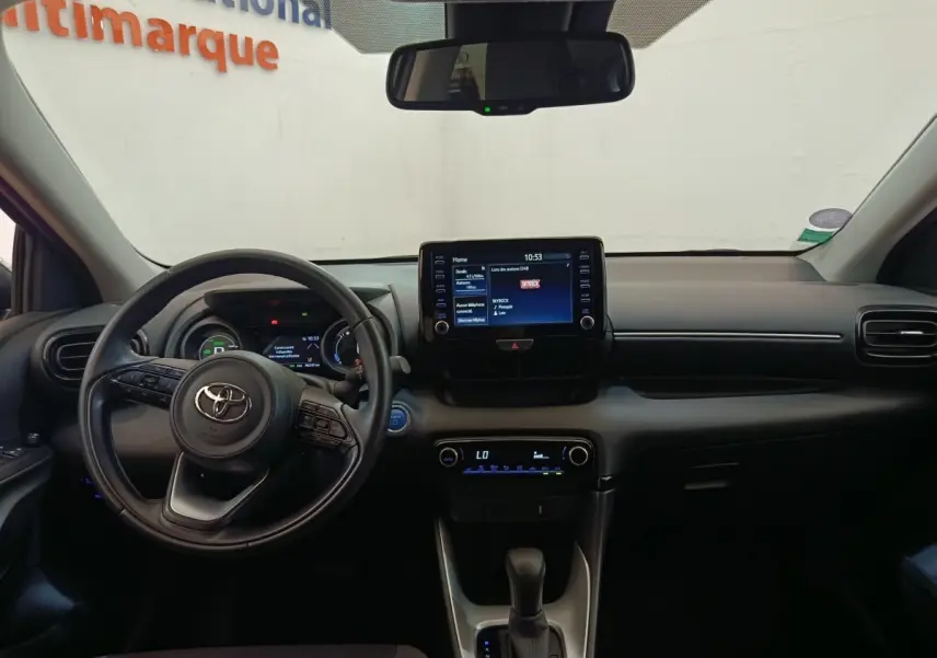 Vue intérieure frontale du tableau de bord noir de la Toyota Yaris Hybride 116h avec écran tactile central et volant cuir multifonctions.