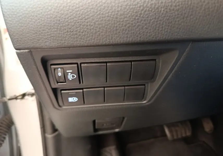 Gros plan sur les commandes de réglage des phares à gauche sous le tableau de bord d'une Toyota Yaris hybride gris clair 2023.