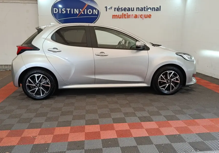 Vue latérale droite d'une Toyota Yaris Hybride 116h Design gris clair, avec jantes alliage et feux arrière distinctifs.
