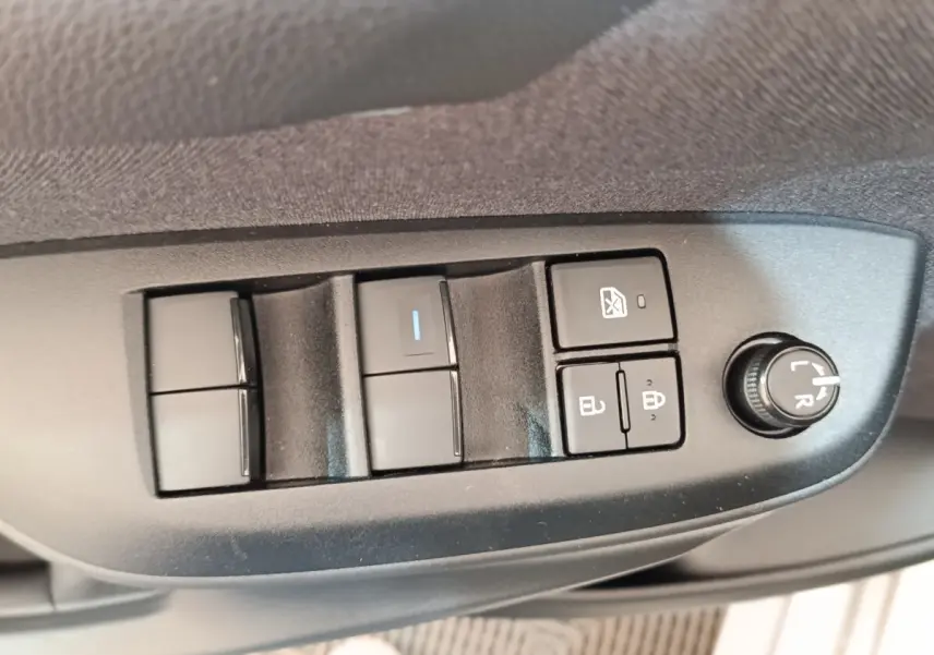 Gros plan sur les commandes de lève-vitres et réglage des rétroviseurs côté conducteur d'une Toyota Yaris hybride gris clair 2023.
