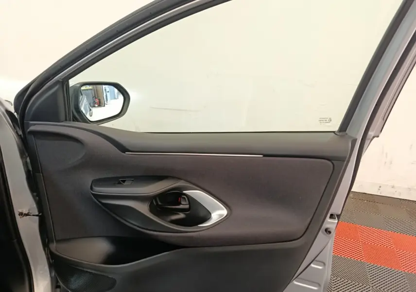 Vue intérieure de la porte avant gauche gris clair de la Toyota Yaris Hybride 116h Design 2023 avec poignée noire et garniture tissu.
