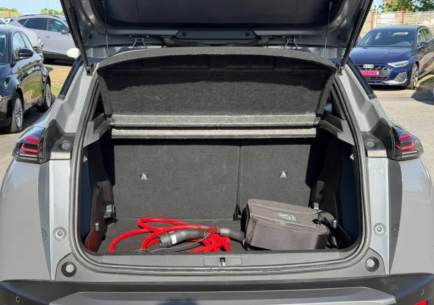 Coffre ouvert en vue arrière d’un Peugeot e-2008 gris Artense avec câble de recharge électrique rouge visible.