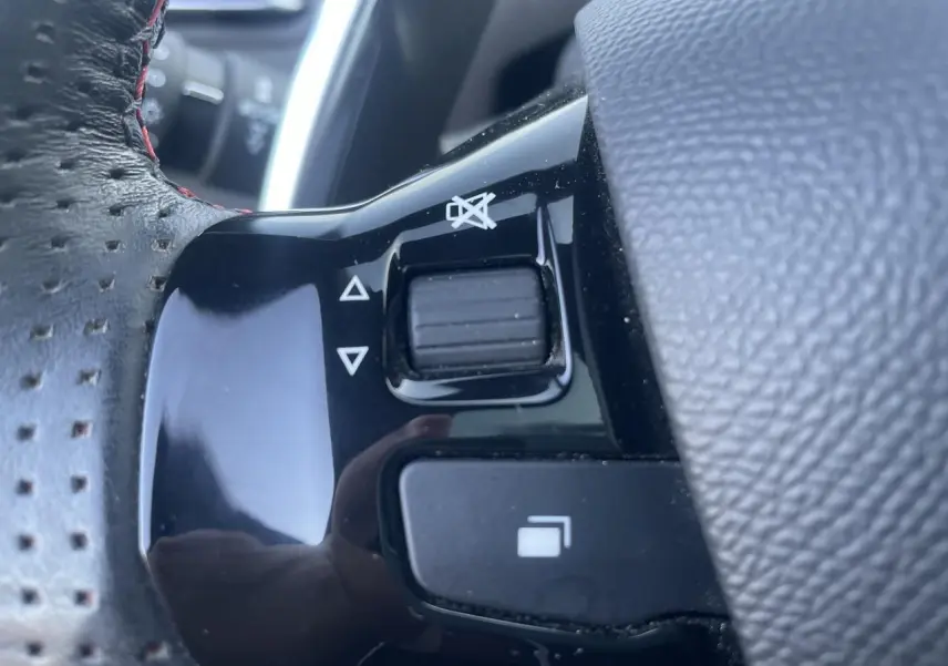 Gros plan sur les commandes noires du volant cuir perforé avec surpiqûres rouges d'une Peugeot 308 SW Bleu Vertigo.