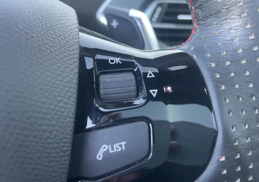 Gros plan sur les commandes au volant en cuir perforé avec surpiqûres rouges de la Peugeot 308 SW GT Pack 2021.