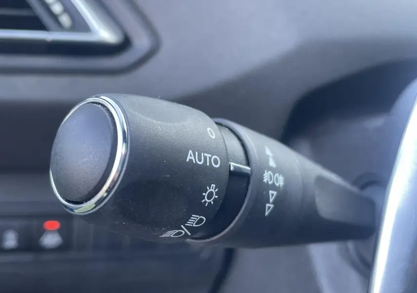 Gros plan sur la commande des feux automatique dans l'habitacle sombre d'une Peugeot 308 SW Bleu Vertigo 2021.